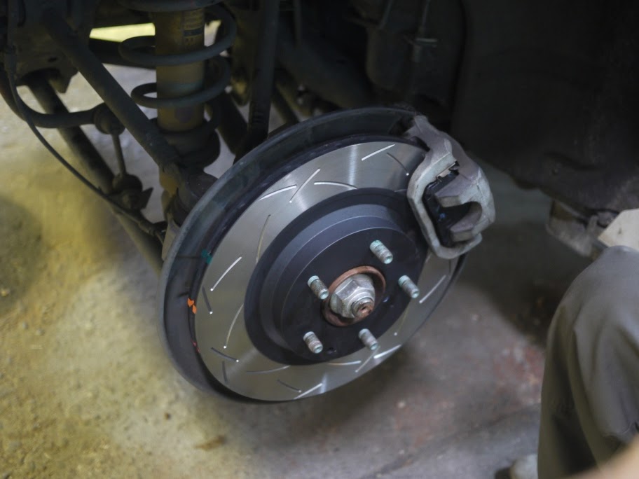 A fresh slotted brake rotor and caliper during a brake job at J&T